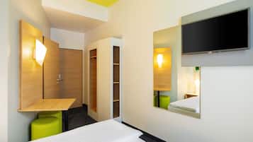 Habitación de hotel con cama, televisor en la pared, espejo y armario.