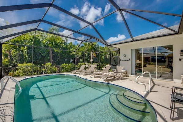 A swimming pool with a glass ceiling, lounge chairs, and a view of greenery. - 16684 Wellington Pet Friendly Pool Home by Beach (Fort Myers)