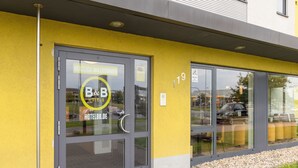 L’entrée d’un hôtel avec une porte en verre, un mur jaune et une enseigne indiquant « B&B HOTELS HOTELBB.DE ».
