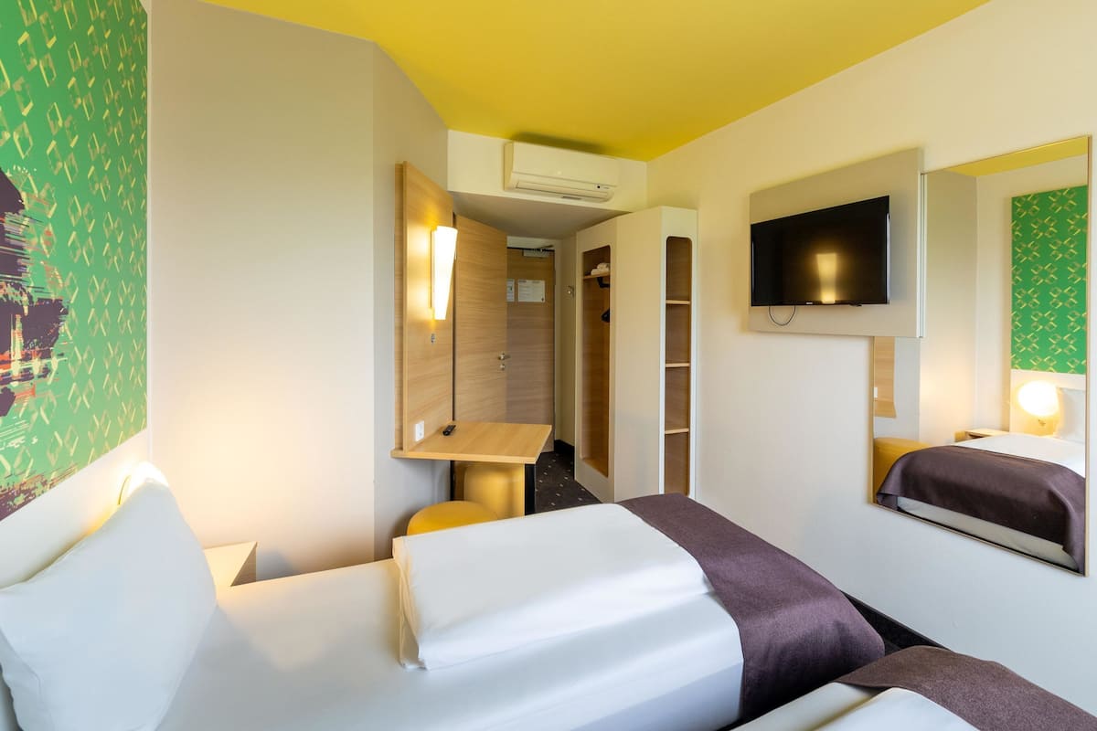 Habitació d'hotel amb dos llits, un televisor, un mirall i un armari.