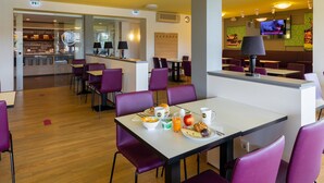 Un restaurant moderne avec des chaises violettes, un comptoir où est affiché le menu et un écran de télévision diffusant une émission.
