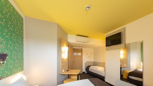 Une chambre d’hôtel avec deux lits, un bureau, un miroir et une télévision.