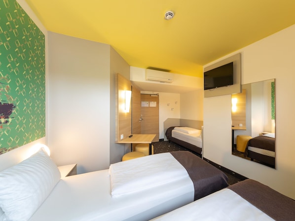 Ein Hotelzimmer mit zwei Betten, einem Schreibtisch, einem Spiegel und einem Fernseher.