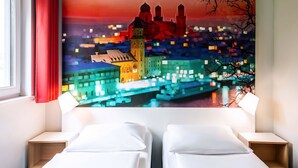 A hotel room with two beds, a large pixelated cityscape painting on the wall, and a window with red curtains. - B&B Hotel Passau-West (Passau)
