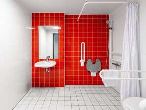 A modern bathroom with a red tiled wall, a white sink, a mirror, a shower, and a toilet. - B&B Hotel Passau-West (Passau)