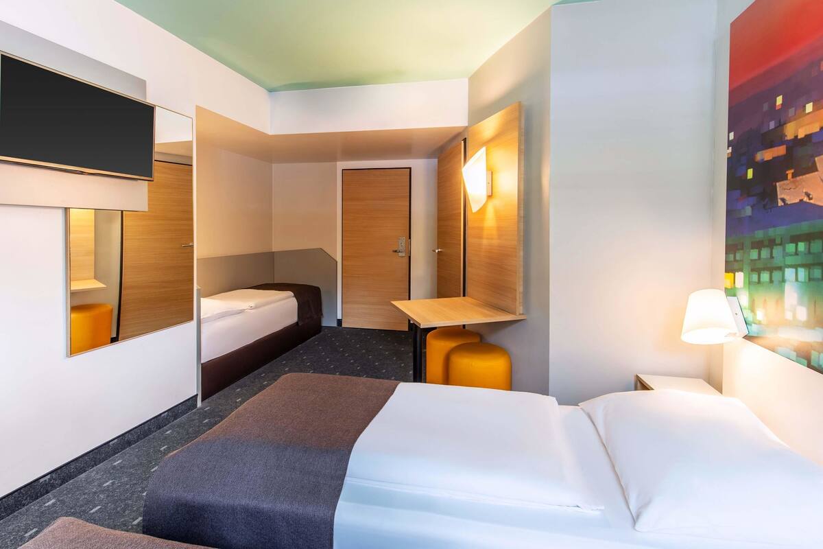 Hotellihuone, jossa on sänky, työpöytä, tuoli, televisio ja taulu seinällä.