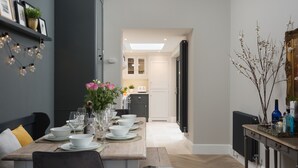 A dining area with a long wooden table set for a meal, a kitchen in the background, and a radiator on the right. - 4 St Martins Lane. Luxurious Central York Town House. Newly refurbished (York)