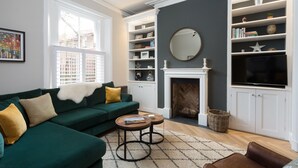 A living room with a green sofa, two round coffee tables, a fireplace, and a bookshelf. - 4 St Martins Lane. Luxurious Central York Town House. Newly refurbished (York)
