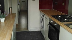 A modern kitchen with a wooden countertop, a washing machine, a stove, and a red backsplash. - Remarkable 3-bed House in Hounslow (Hounslow)