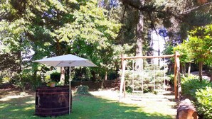 A wooden swing set in a lush garden with a large umbrella and a barrel.