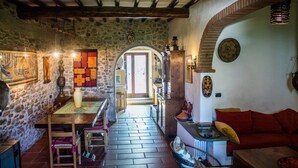 A cozy interior with a stone wall, wooden beams, a dining area, and a red sofa.