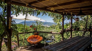 A wooden deck with a bench and a hanging chair, surrounded by lush greenery and potted plants.