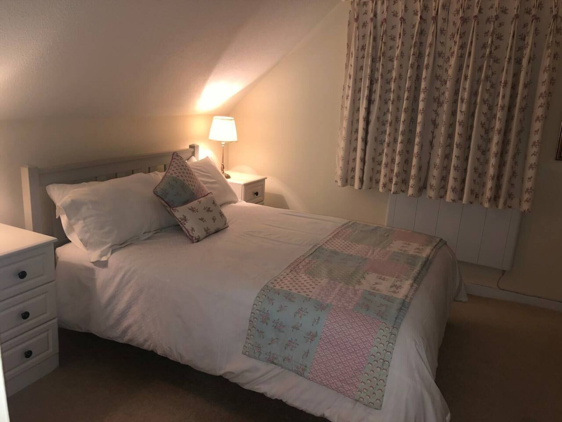 Una cama bien hecha con colcha, una lámpara de noche y una mesita de noche con cajones.