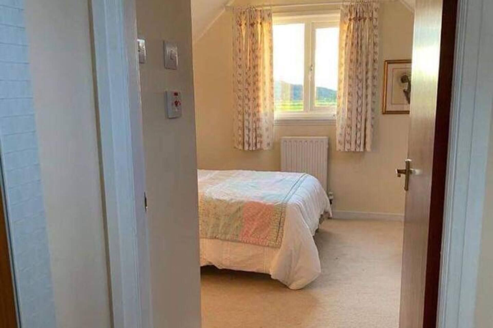 Een slaapkamer met een bed, een radiator en een raam met gordijnen.