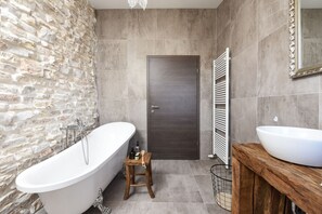 A bathroom with a freestanding bathtub, a wooden stool, a door, and a vanity with a mirror. - Villa Trabakul (Razanac)