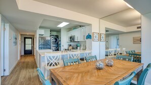 Uma cozinha moderna com armários brancos, uma ilha central e uma área de jantar com mesa de madeira e cadeiras azuis.