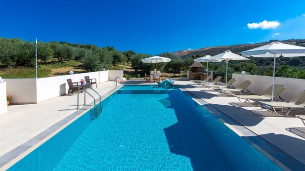 Una piscina con lettini e ombrelloni, circondata da ulivi e con vista sulle colline.