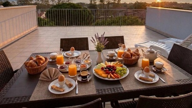 A breakfast setup on a terrace with a view of the sea at sunset, including croissants, fruits, and beverages. - Wonderful attic flat with sea view (Rosolina Mare)