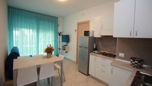 A compact kitchen with a refrigerator, microwave, and stove. There is a dining table with chairs and a vase of flowers. - Wonderful attic flat with sea view (Rosolina Mare)