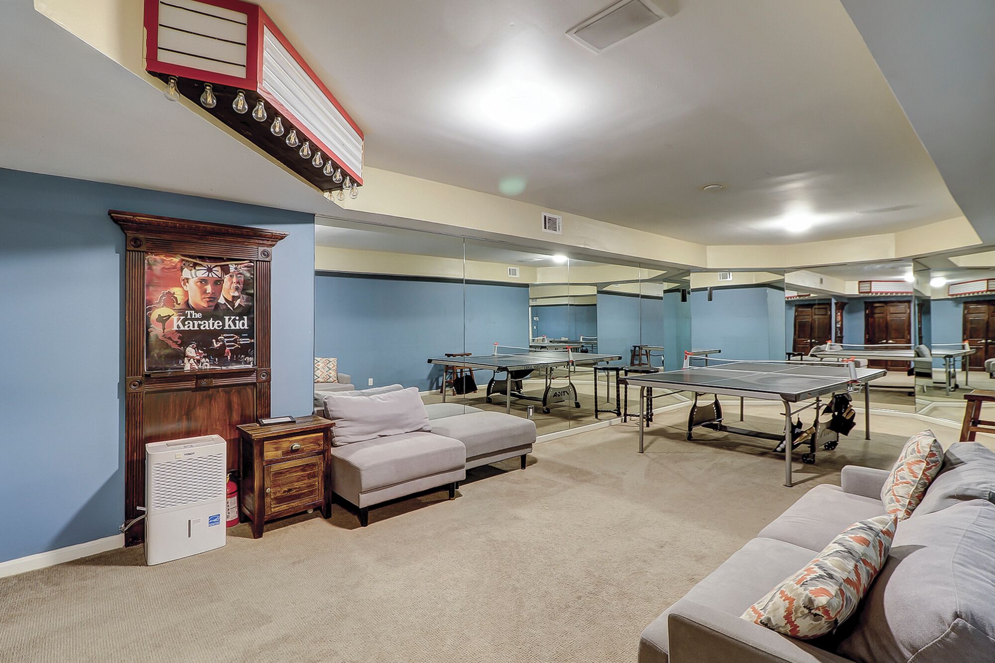 A room with multiple ping pong tables, a sofa, a small cabinet, and a poster on the wall.
