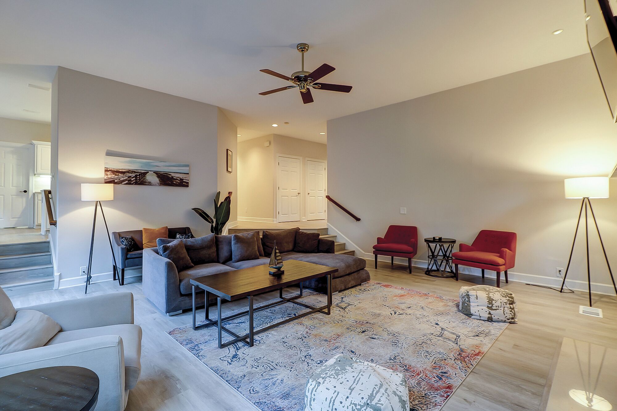 A spacious living room with a sofa set, a coffee table, and two red armchairs. A ceiling fan and a floor lamp are visible.