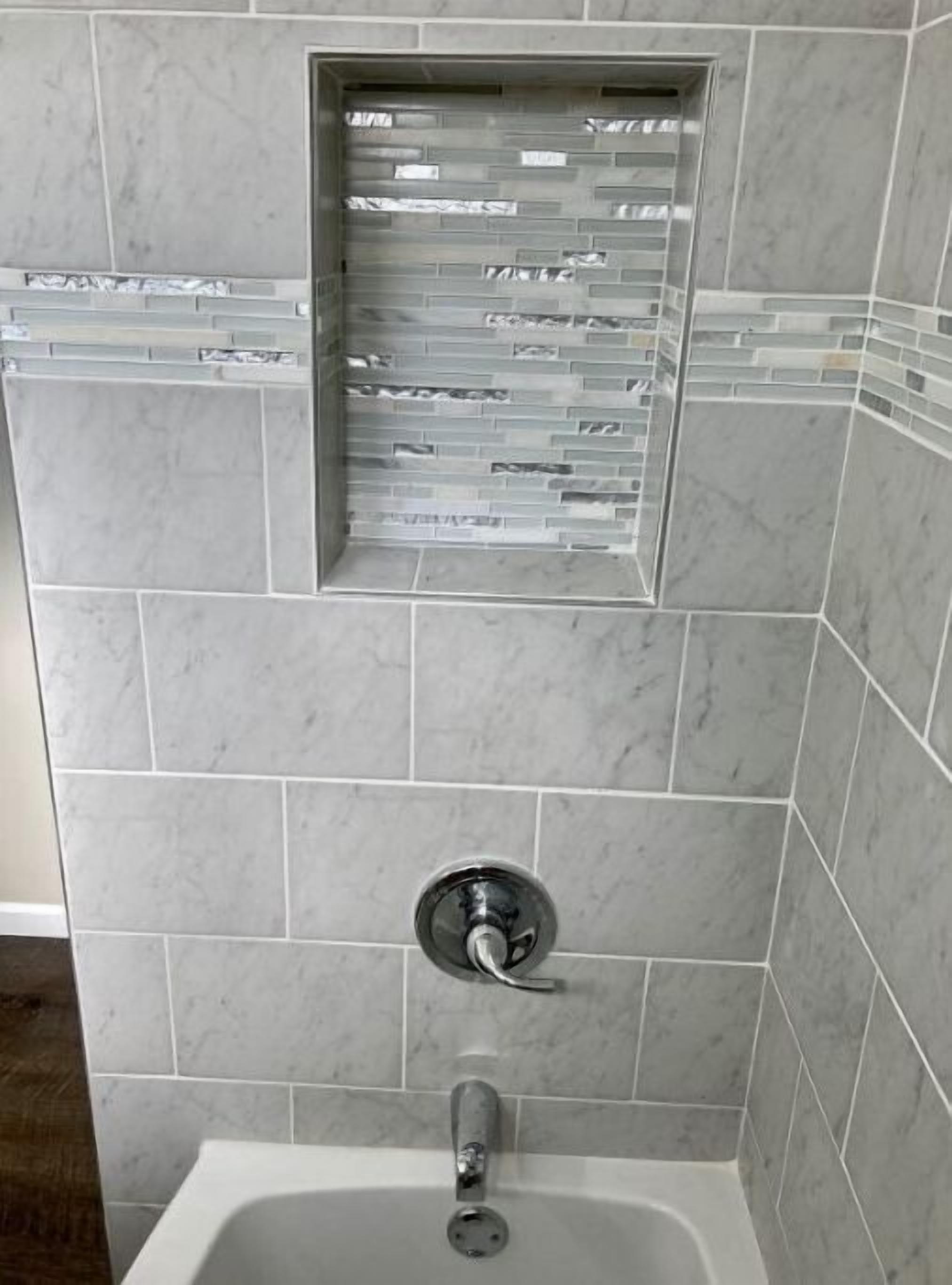Uma casa de banho com zona de duche, um prateleira de vidro embutida e uma banheira.