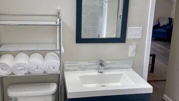Ein Badezimmer mit einer weißen Toilette, einem blauen Waschtisch mit Spiegel und einem Handtuchhalter mit ordentlich gefalteten Handtüchern.