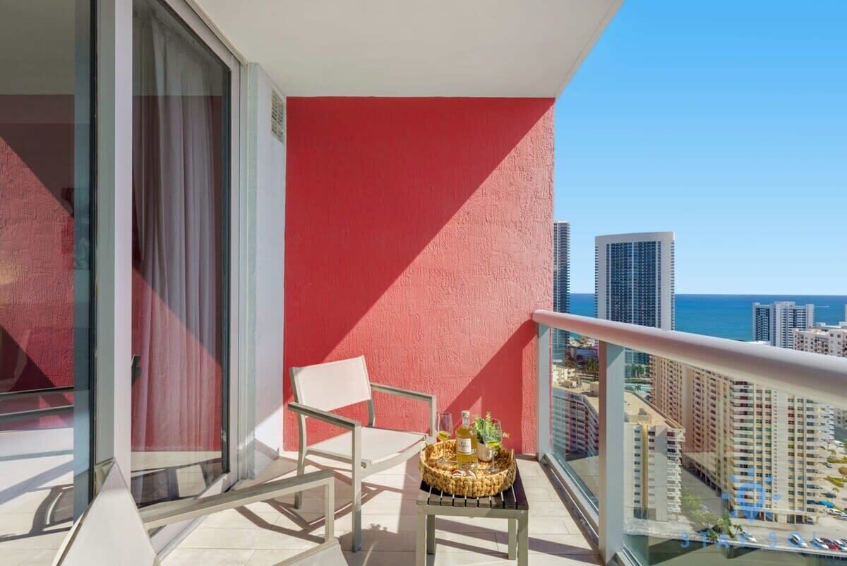 A balcony with a red wall, a white chair, and a table with drinks and a plant.