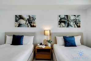 A hotel room with two beds, a nightstand with a lamp, and artwork on the wall.