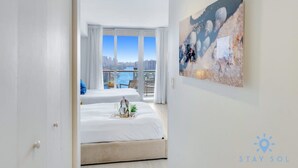 Ett hotellrum med ett stort fönster som ger utsikt över staden, en säng med ett dekorativt brickbord och en tavla på väggen.