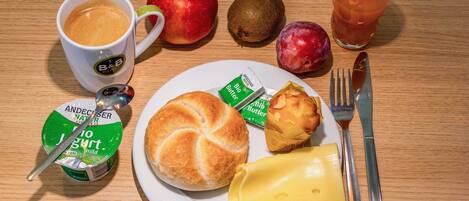 Un plato de desayuno con un croissant, queso, mantequilla, un muffin, una manzana, un kiwi, un vaso de jugo y una taza de café.