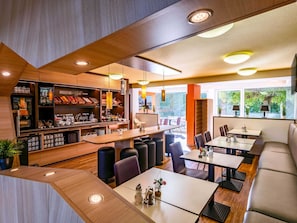 Un restaurant moderne doté d’un bar, de tables et de grandes fenêtres offrant une vue sur l’extérieur.