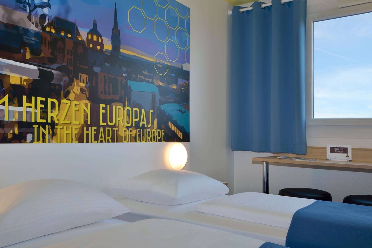 Une chambre d’hôtel avec un lit, une table de chevet, un bureau et une grande affiche au mur.