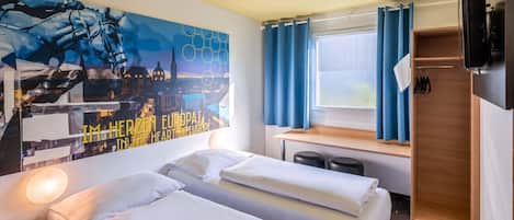 A hotel room with two beds, a desk, a TV, and a large cityscape painting on the wall.