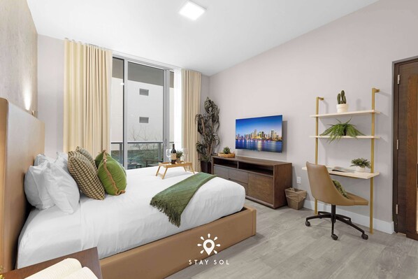 Une chambre d’hôtel moderne équipée d’un lit, d’un bureau, d’une chaise, d’une télévision et d’un tableau représentant un paysage urbain.