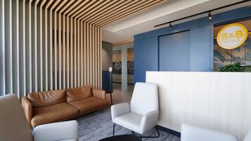Un área de recepción moderna con techo de listones de madera, un mostrador de recepción y un espacio de espera con sillas de cuero y blancas.