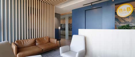 A modern reception area with a wooden slatted ceiling, a reception desk, and a seating area with leather and white chairs.