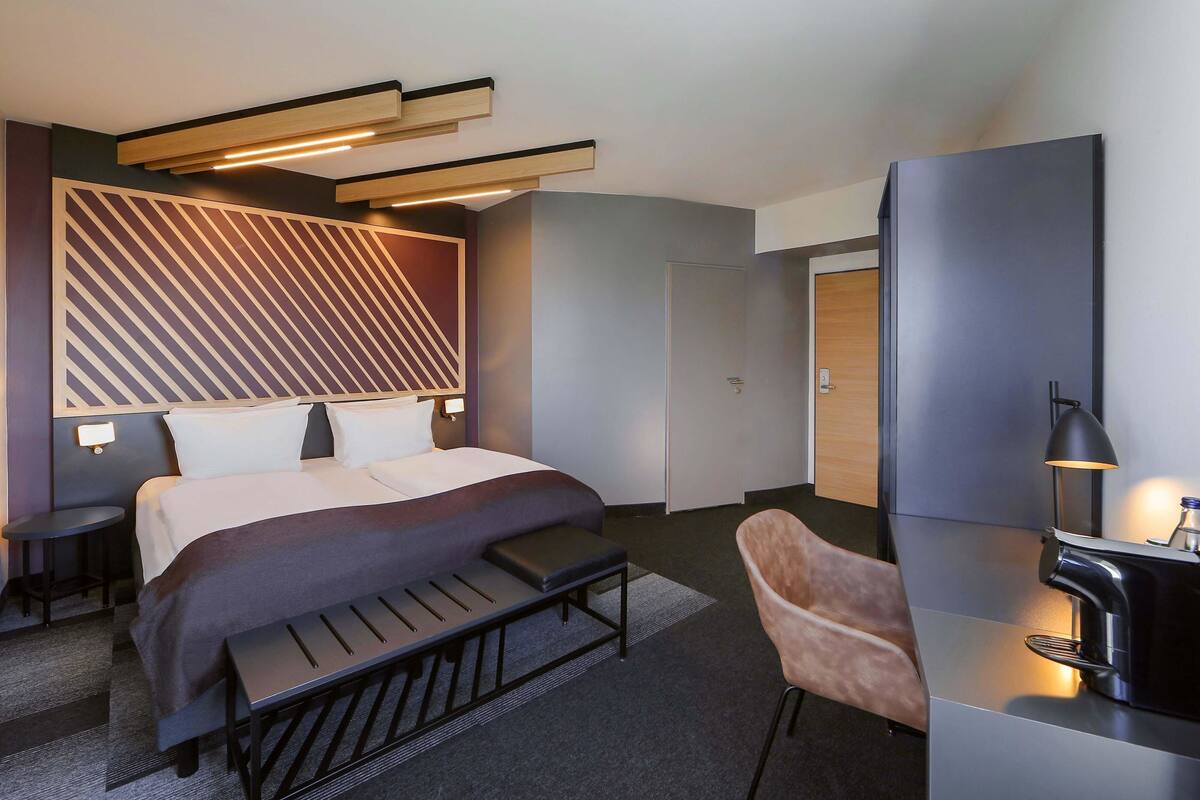 Una habitación de hotel moderna con cama, mesitas de noche, escritorio, silla y cafetera.
