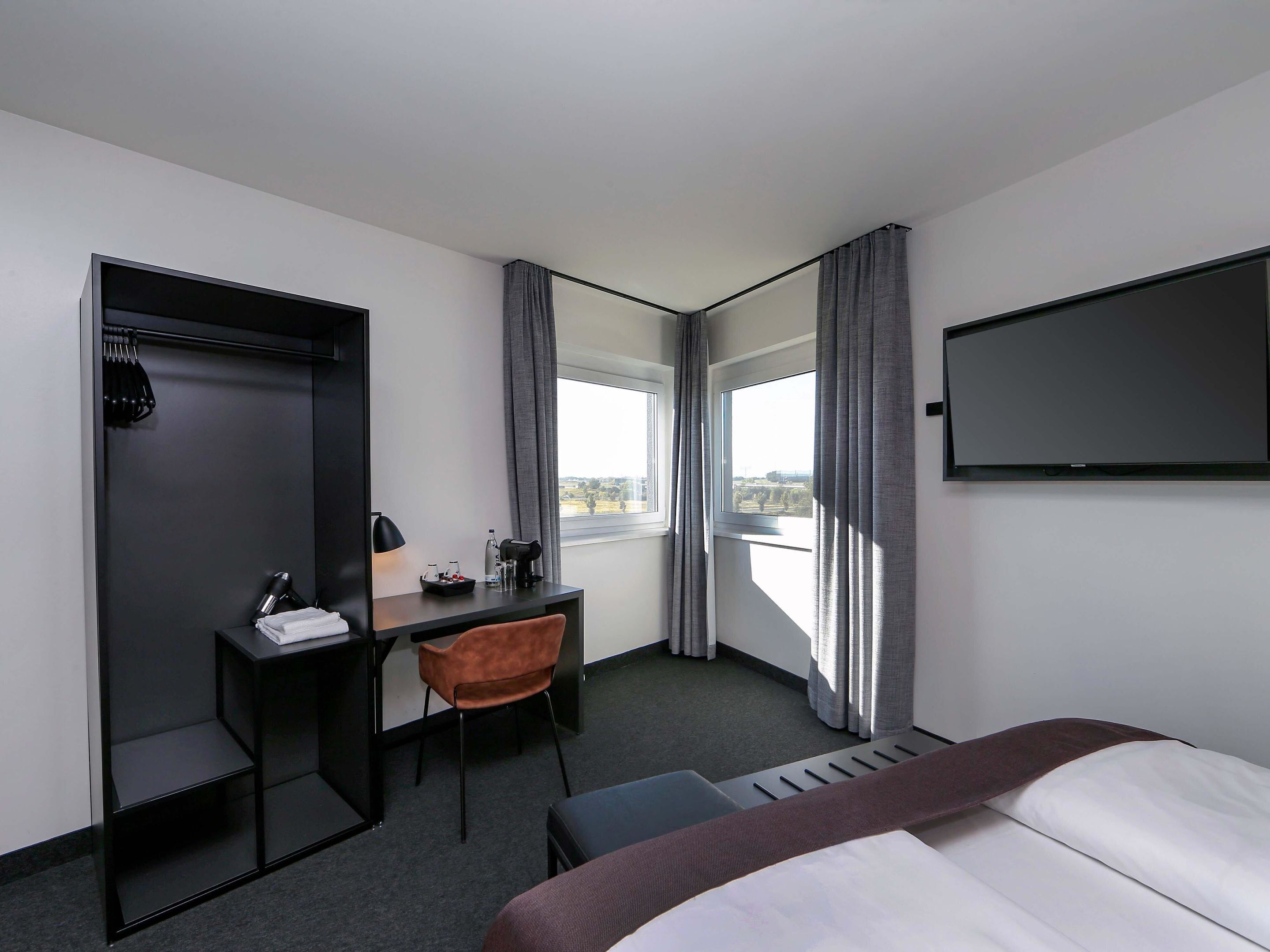 Ein Hotelzimmer mit einem Bett, einem Schreibtisch mit Stuhl, einem Fernseher und einem Fenster mit Vorhängen.