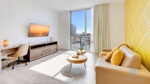Une chambre d’hôtel moderne dotée d’une grande fenêtre, d’un bureau, d’un canapé et d’un téléviseur fixé au mur.