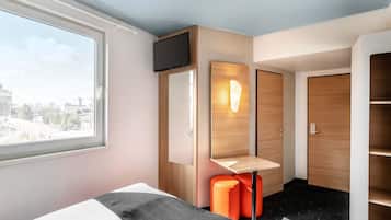 Habitación de hotel con cama, televisor montado en la pared, armario de madera y ventana con vista a la ciudad.
