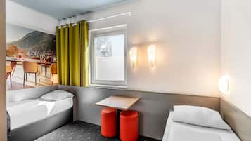 Ein Hotelzimmer mit einem Bett, einem kleinen Tisch, zwei roten Hocker, einem Fenster mit Vorhängen und Blick auf Berge und Stadt.
