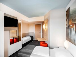 Una habitación de hotel moderna con una cama, un escritorio, una silla, un televisor y un cuadro en la pared.