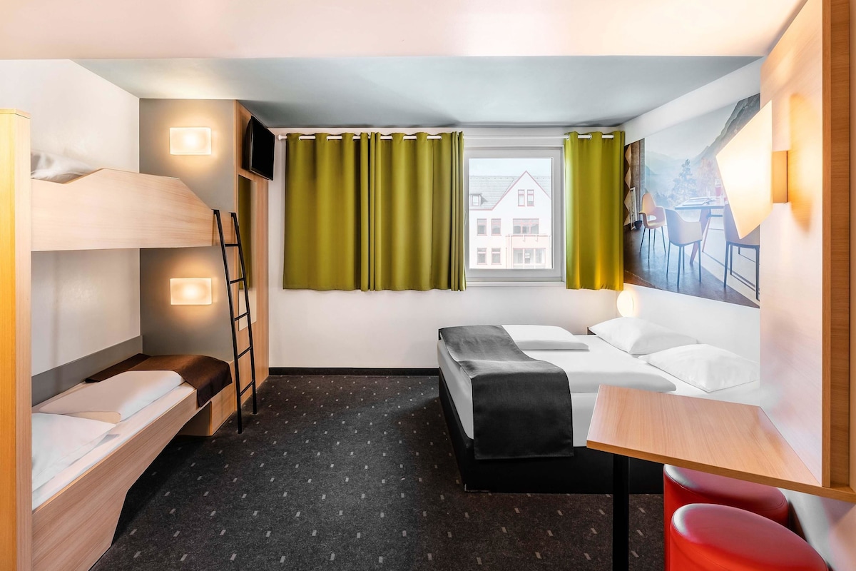 Una camera d'albergo compatta con un letto a castello, un letto singolo, una scrivania e una sedia.