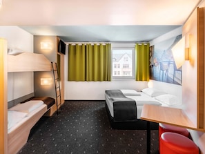 A compact hotel room with a bunk bed, a single bed, a desk, and a chair.