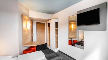 Ein modernes Hotelzimmer mit einer Couch, einem an der Wand montierten Fernseher und einer Holztür.