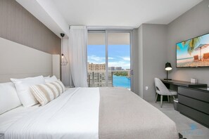 Una habitación de hotel moderna con una cama grande, un escritorio y vistas a la ciudad y a la piscina.
