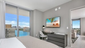 A hotel room with a bed, desk, chair, and a painting of a beach scene. - Corner Balcony:-Enjoy 360° Views+ Near Beach+ Pool (Hollywood)