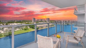 A balcony with a view of a sunset over a body of water, surrounded by modern buildings. - Corner Balcony:-Enjoy 360° Views+ Near Beach+ Pool (Hollywood)