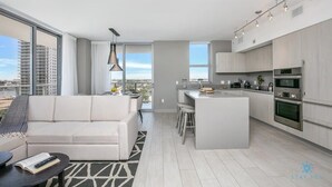 A modern apartment with a living area, kitchen, and large windows offering city views. - Corner Balcony:-Enjoy 360° Views+ Near Beach+ Pool (Hollywood)